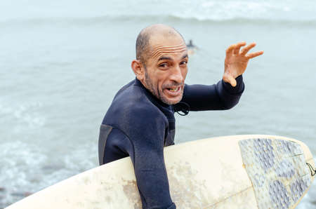 Portrait of mature surfer standing on the beach with a surfboard in hands.の写真素材