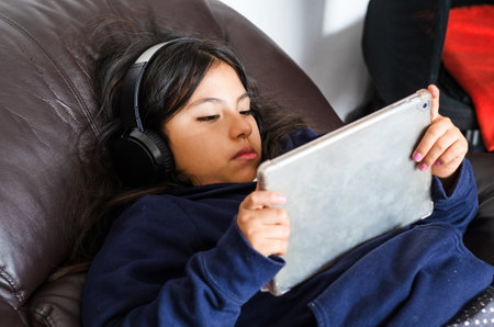 Small girl school pupil wears headphones conference calling studying online with remote tutor from...
