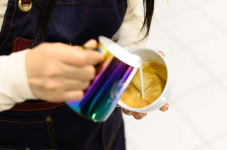 Hands of barista making latte or cappuccino coffee pouring milk, making latte art.の写真素材