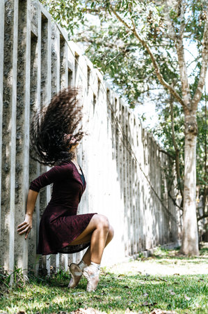 Beautiful young graceful ballerina in black dress sitting and on tiptoe in park looking up.の写真素材