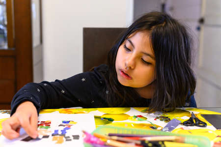 Little girl gluing colored papers for her homework.