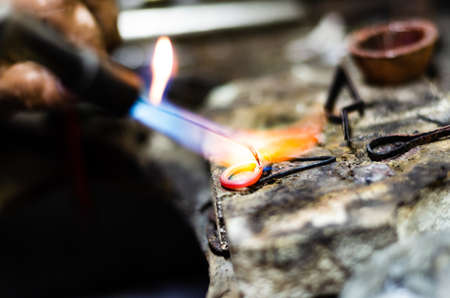 Close up of jeweler making golden ring with flame torch.