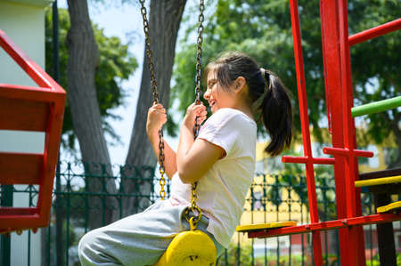 happy little hispanic girl child having fun to playing in the park in summer time with smile and laughing healthy, Adorable girl having fun on a swing on summer. happy vacation lifestyle concept.の写真素材
