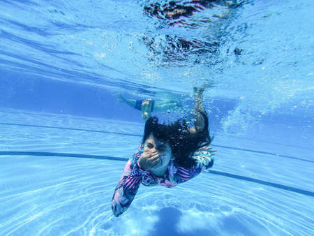 little girl creates bubbles under water in the pool.の写真素材