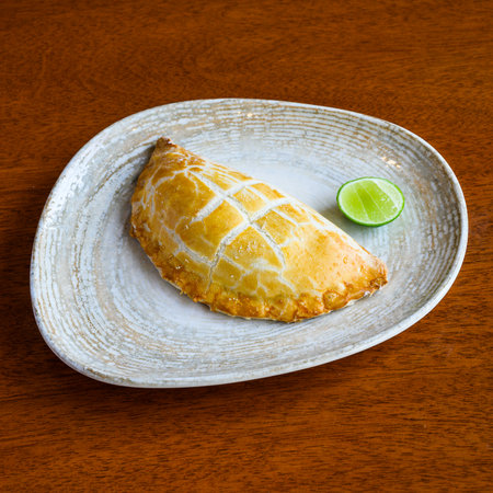 Fresh baked empanada with lime on ceramic plate