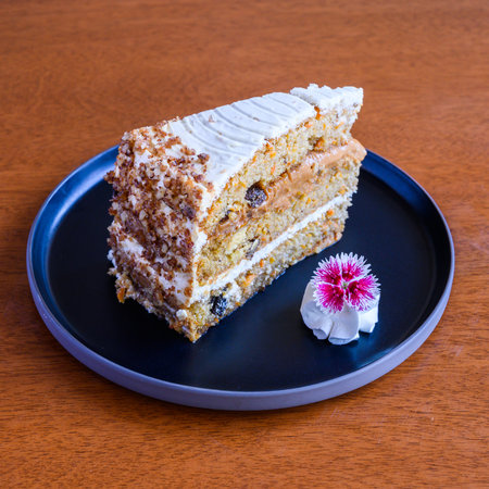 Delicious slice of carrot cake with cream cheese frosting on dark plate