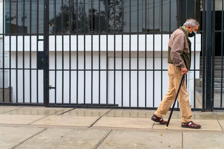 Elderly man walking with cane and mask on city streetの写真素材