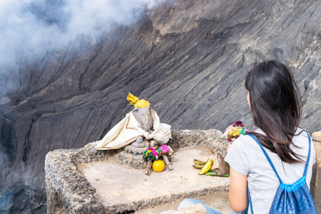 Young woman bringing offerings to a hindu deity statue at mount bromo crater rim in indonesiaの写真素材