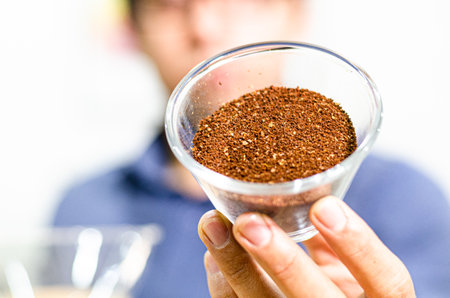 Barista holding ground coffee beans in a transparent bowlの写真素材