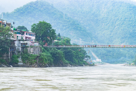 Tourists crossing a suspension bridge over river ganges in rishikesh, india