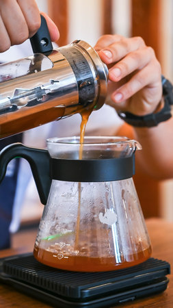 Barista pouring coffee from french press into glass server on kitchen scale