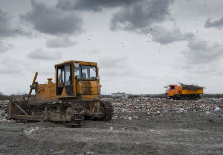 bulldozer working on landfill with birds in the sky