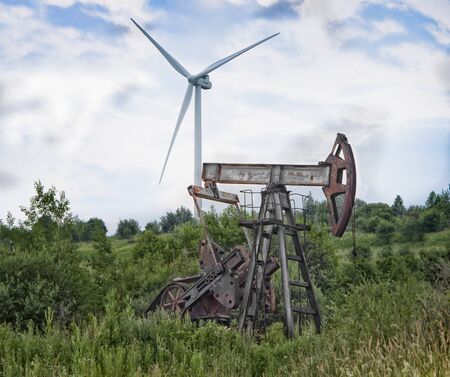 Operating oil and gas well, profiled on blue sky with clouds and wind turbine