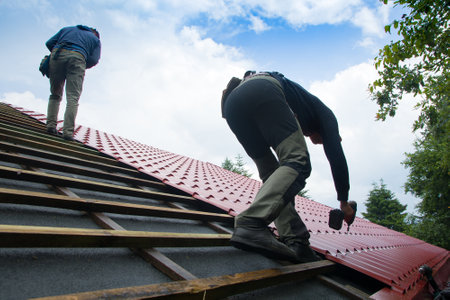 Roofers working on roof structure of building on construction site,Roofer using air or pneumatic nail gun and installing Metal Sheet on top new roof.の写真素材