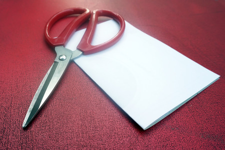 Red scissor with white paper on red wooden backgroundの写真素材