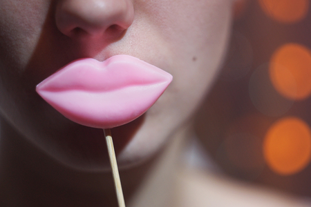 Beauty joyful Young Funny fashion model Girl holding big pink lips on a stick smiling, Beauty concept. On bokeh lights background.の写真素材