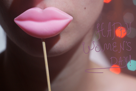 Beauty joyful Young Funny fashion model Girl holding big pink lips on a stick smiling, 8 March sign Happy Women's Day concept. On bokeh lights background.の写真素材