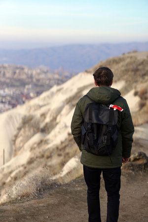 Young Male Tourist Hiking with Backpacks on Top of Rocky Canyon Valley in Front of a city Goreme Cappadocia view in the Mountains of National Park.の写真素材