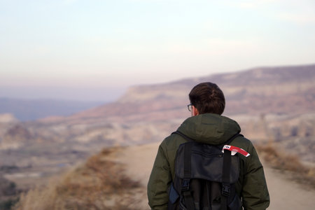 Young Male Tourist Hiking with Backpacks on Top of Rocky Canyon Valley in Front of a city Goreme Cappadocia view in the Mountains of National Park.の写真素材