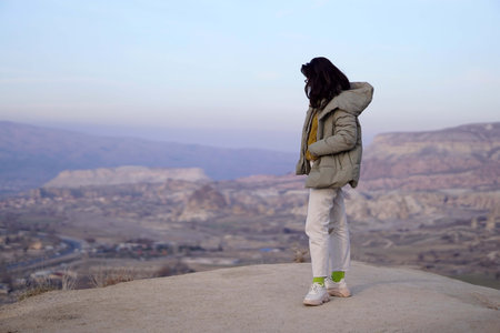 Young Female Tourist Hiking on Top of Rocky Canyon Valley in Front of a city Goreme Cappadocia view...