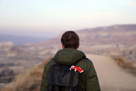Young Male Tourist Hiking with Backpacks on Top of Rocky Canyon Valley in Front of a city Goreme Cappadocia view in the Mountains of National Park.の写真素材