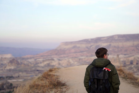 Young Male Tourist Hiking with Backpacks on Top of Rocky Canyon Valley in Front of a city Goreme Cappadocia view in the Mountains of National Park.の写真素材