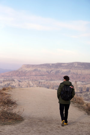 Young Male Tourist Hiking with Backpacks on Top of Rocky Canyon Valley in Front of a city Goreme Cappadocia view in the Mountains of National Park.の写真素材