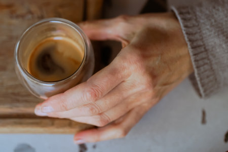 Close-up image of a glass cup of coffee held in woman hand. Caffeine and restaurant for cappuccino. Customer, hospitality for female person, morning and barista for breakfast. Hand-roasted coffee.の写真素材