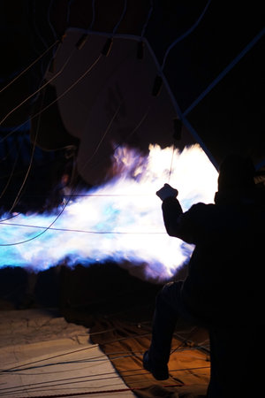 Bright blue flame from a hot air balloon burner at night, illuminating ropes and fabric while a person controls the fire, creating a dramatic and powerful aviation scene.の写真素材