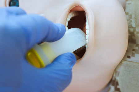 A gloved hand inserting an oropharyngeal airway tube into a medical training mannequin in camouflage uniform for airway management practice. Correct demonstration of airway tube placement during tccc.の写真素材