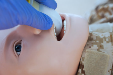 A gloved hand inserting an oropharyngeal airway tube into a medical training mannequin in camouflage uniform for airway management practice. Correct demonstration of airway tube plの写真素材