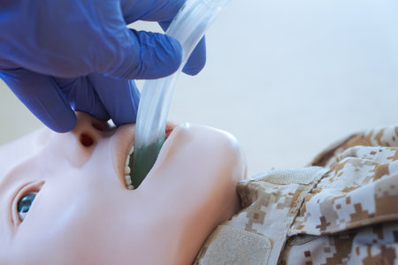 Medical training mannequin in camouflage uniform during insertion of an i-gel supraglottic airway device. The procedure illustrates airway management placement as part of a militarの写真素材