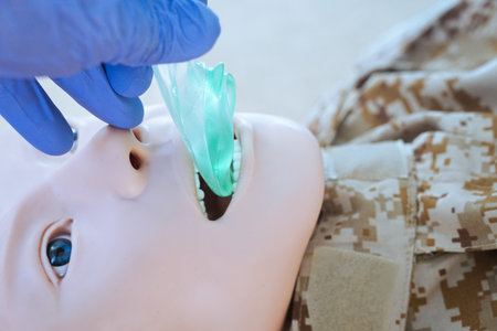 Medical training mannequin in camouflage uniform during insertion of an i-gel supraglottic airway device. The procedure illustrates airway management placement as part of a military medical simulationの写真素材