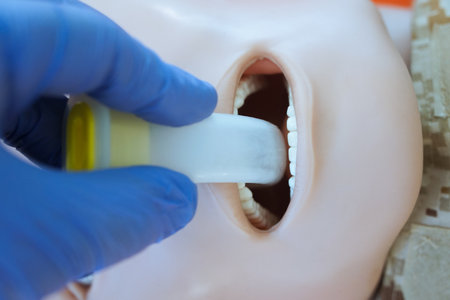 A gloved hand inserting an oropharyngeal airway tube into a medical training mannequin in camouflage uniform for airway management practice. Correct demonstration of airway tube placement during tccc.の写真素材