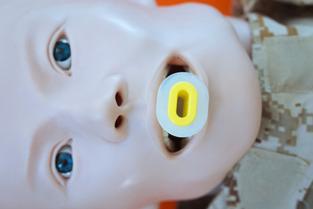 Medical training mannequin in a camouflage uniform with an oropharyngeal airway tube inserted for airway management practice. This setup represents airway tube placement during a TCCC training.の写真素材