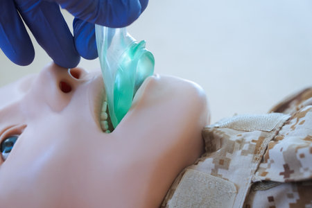 Medical training mannequin in camouflage uniform during insertion of an i-gel supraglottic airway device. The procedure illustrates airway management placement as part of a military medical simulationの写真素材