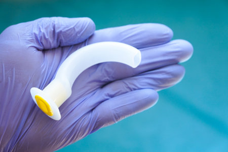 Oropharyngeal airway tube held in a gloved hand, ready for emergency use. Medical equipment for airway management, resuscitation, anesthesia, and first aid training.の写真素材