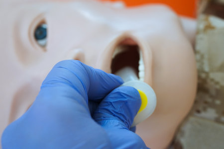 A gloved hand inserting an oropharyngeal airway tube into a medical training mannequin in camouflage uniform for airway management practice. Correct demonstration of airway tube placement during tccc.の写真素材