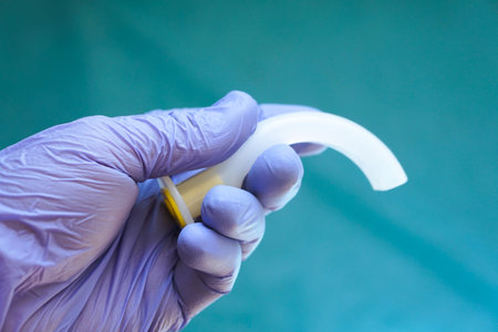 Oropharyngeal airway tube held in a gloved hand, ready for emergency use. Medical equipment for airway management, resuscitation, anesthesia, and first aid training.の写真素材