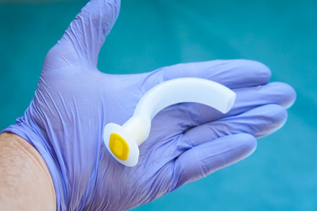 Oropharyngeal airway tube held in a gloved hand, ready for emergency use. Medical equipment for airway management, resuscitation, anesthesia, and first aid training.の写真素材