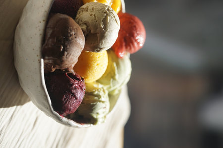 Close up of assorted colorful ice cream and sorbet scoops served in a rustic ceramic bowl on a wooden table: summer dessert, gourmet frozen treat, natural food, cafe or restaurant menu concept.の写真素材