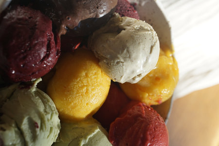 Close up of assorted colorful ice cream and sorbet scoops served in a rustic ceramic bowl on a wooden table: summer dessert, gourmet frozen treat, natural food, cafe or restaurant menu concept.の写真素材