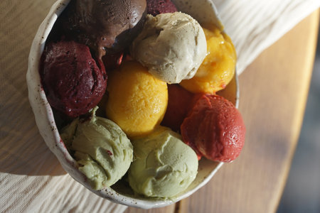 Close up of assorted colorful ice cream and sorbet scoops served in a rustic ceramic bowl on a wooden table: summer dessert, gourmet frozen treat, natural food, cafe or restaurant menu concept.の写真素材