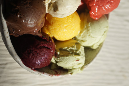 Close up of assorted colorful ice cream and sorbet scoops served in a rustic ceramic bowl on a wooden table: summer dessert, gourmet frozen treat, natural food, cafe or restaurant menu concept.の写真素材
