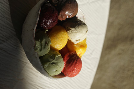 Close up of assorted colorful ice cream and sorbet scoops served in a rustic ceramic bowl on a wooden table: summer dessert, gourmet frozen treat, natural food, cafe or restaurant menu concept.の写真素材