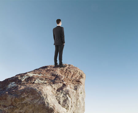 Businessman in suit  standing on rockの写真素材