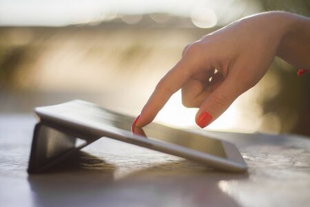 woman hand pushing on a digital tablet at sunrise, shallow depth of fieldの写真素材
