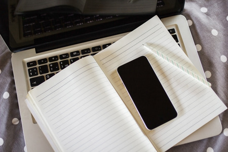 blank cell phone, diary and laptop on the bedの写真素材