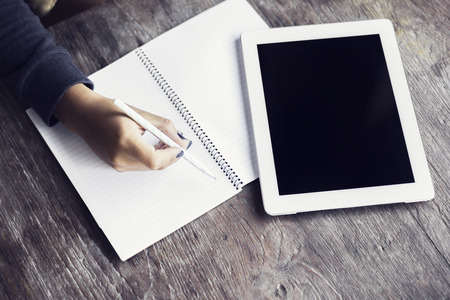 Girl hand with pencil, blank diary and digital tablet on a wooden table