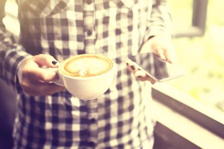 Hipster girl keeping a cappuccino and cell phoneの写真素材